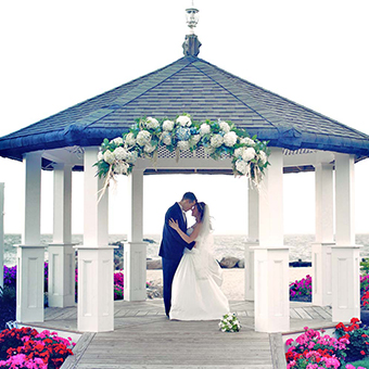 Bride and groom embrace in the gazebo decorated with flowers. 